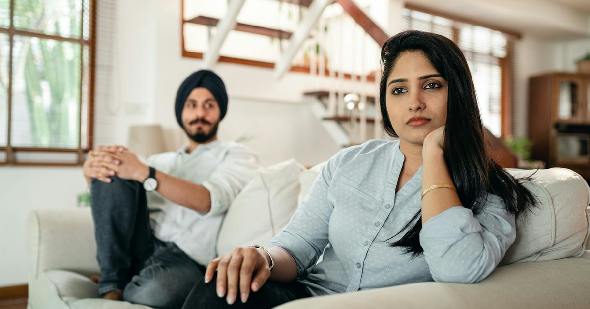 Offended Indian woman sitting on sofa with husband on another end and looking away while having argument