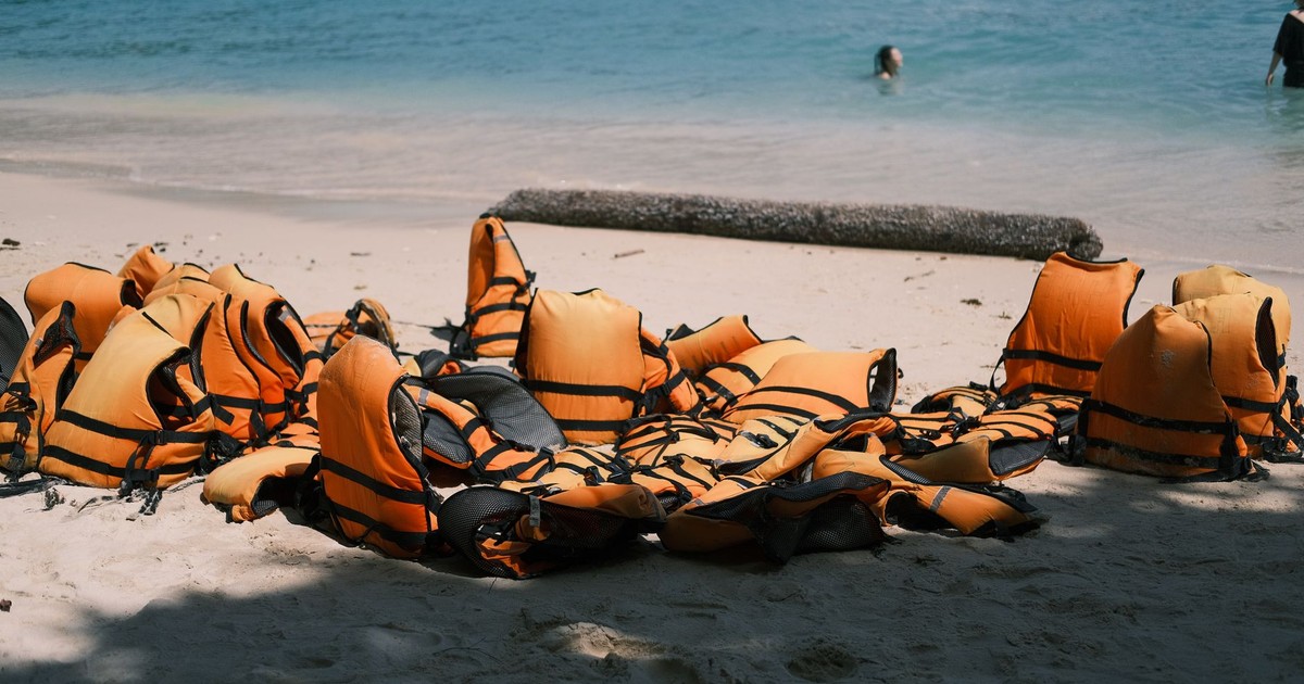 Bright orange life jackets scattered on a sandy beach near the ocean, embodying summer safety and adventure.