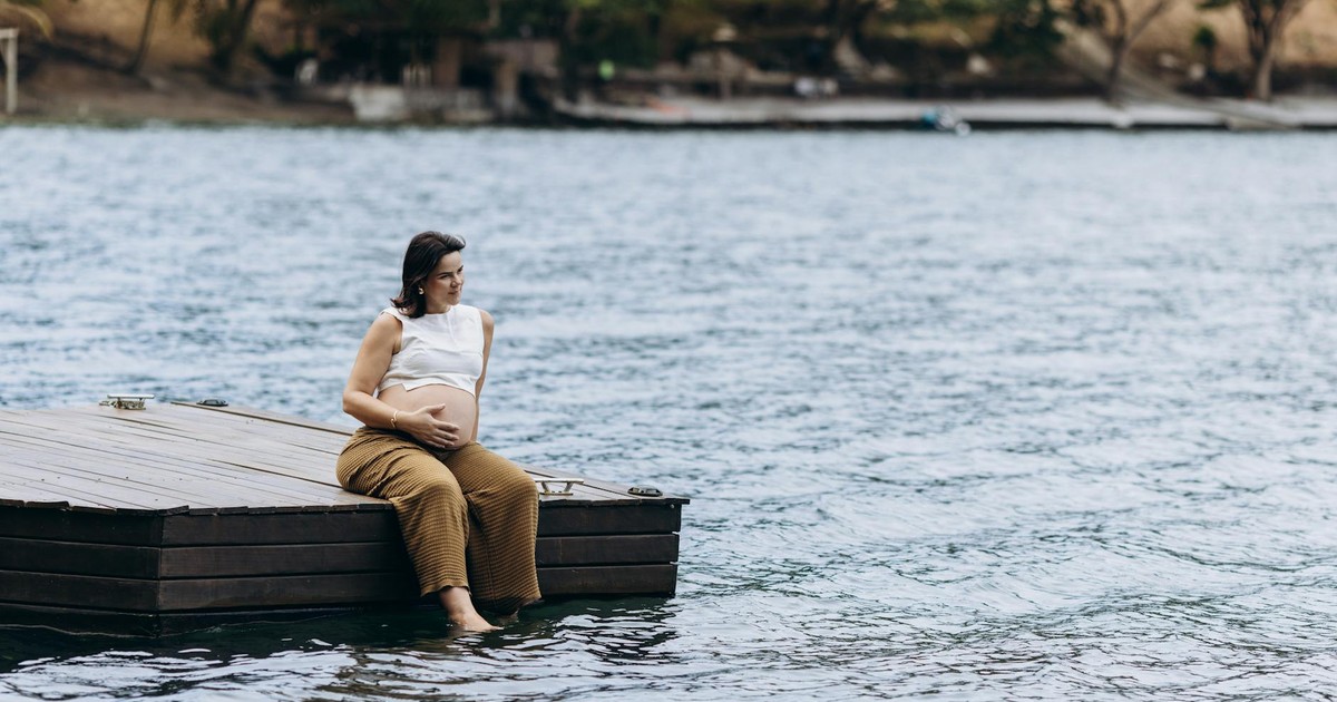 Expectant mother enjoying serene lake view while sitting on a dock.