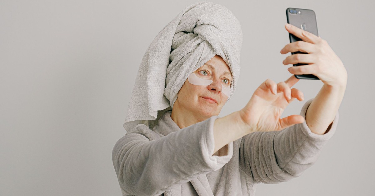 Woman in a bathrobe with skincare pads taking a selfie, promoting self-care and relaxation.