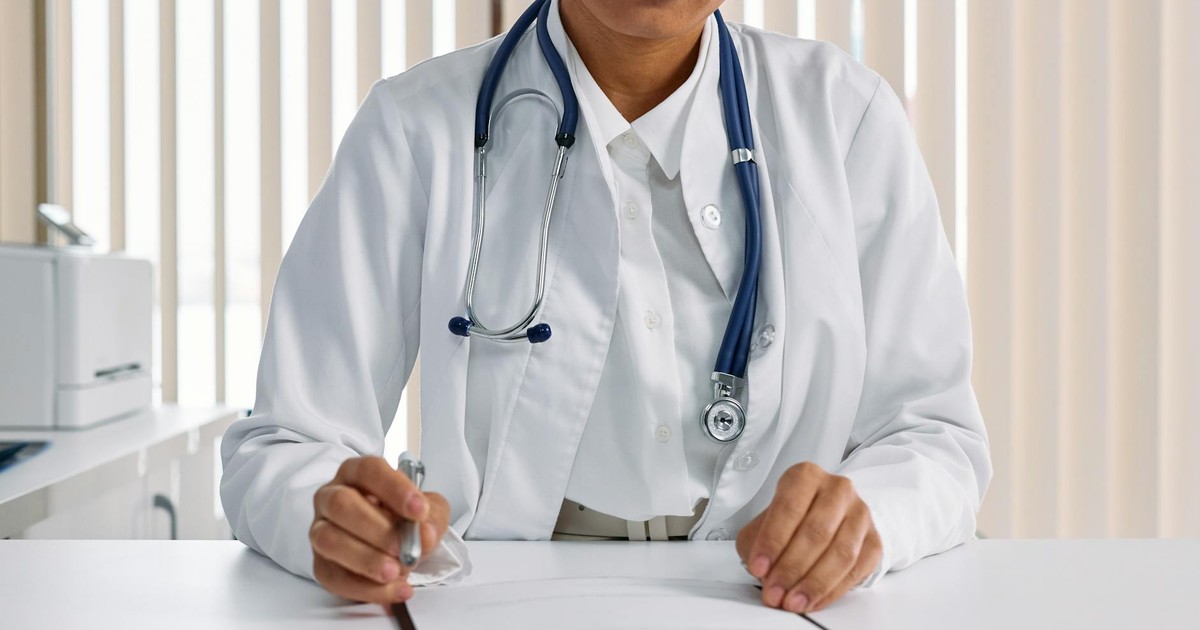 A focused doctor with stethoscope recording patient details in an office setting.