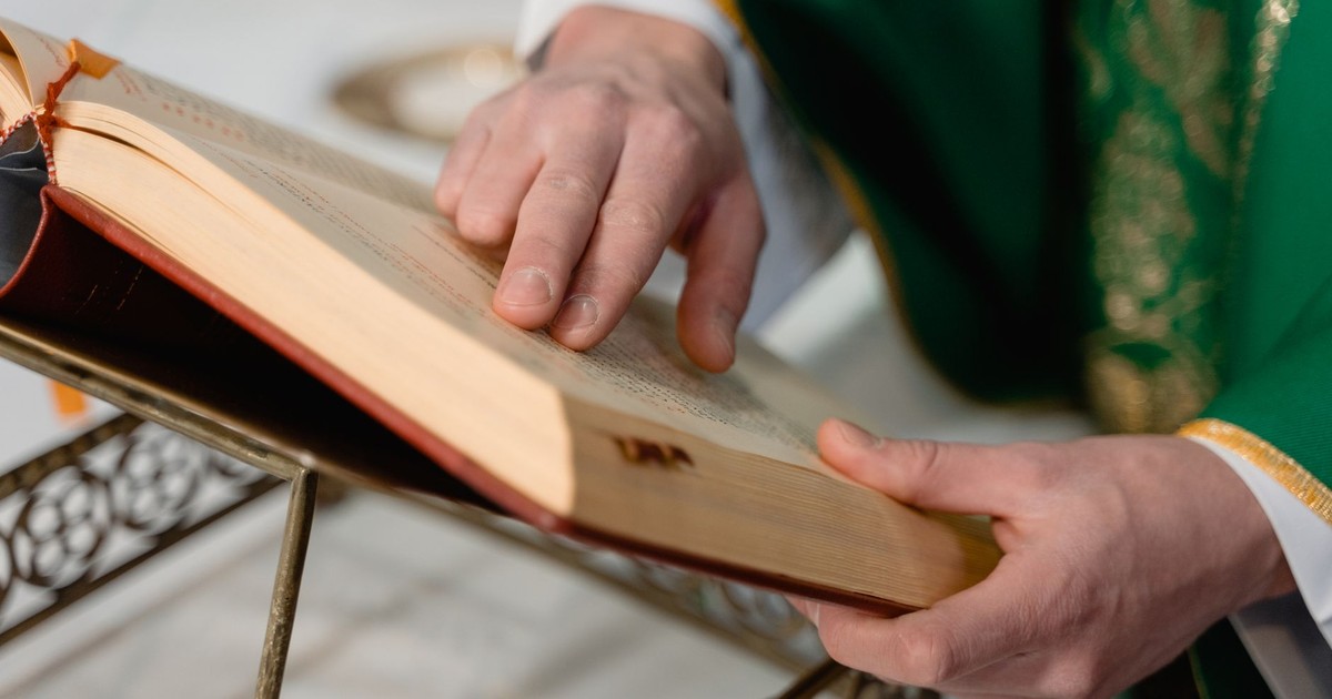 A priest in green robes reads from the Holy Bible, highlighting a moment of worship.