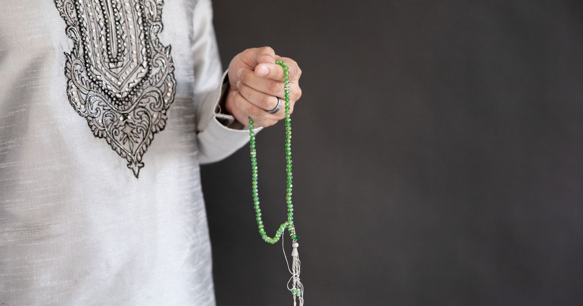Close-up of a person holding traditional Islamic prayer beads against a dark background.