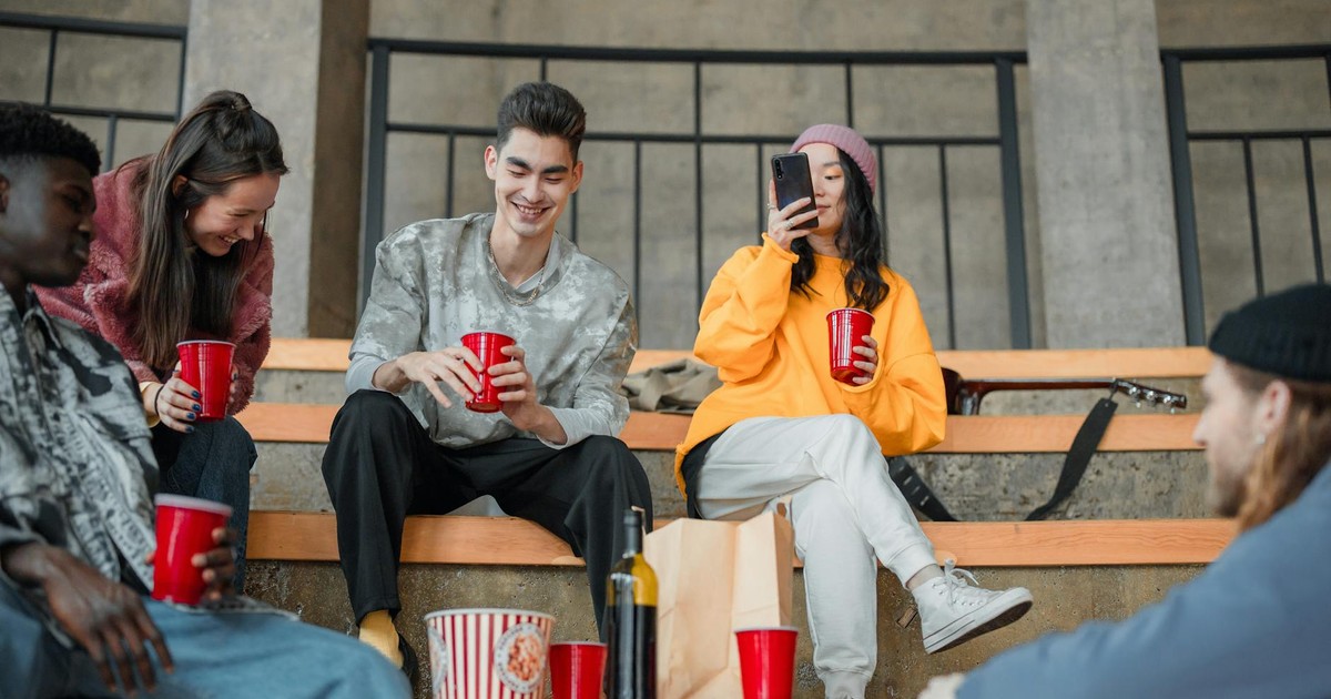 A diverse group of young friends socializing outdoors with drinks and fun vibes.