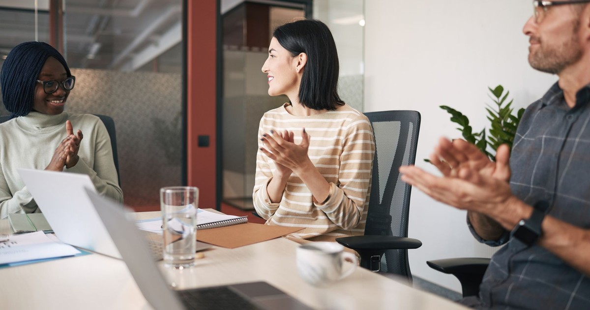 A diverse group of colleagues clapping during a meeting in a modern office.