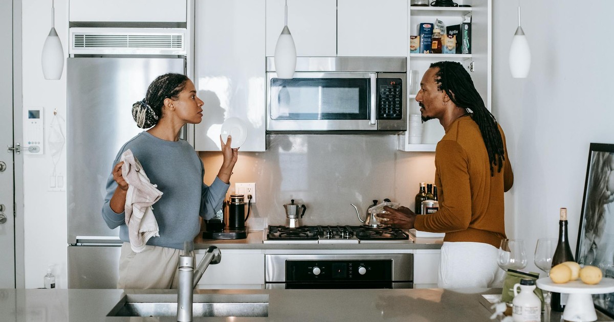 Young black woman talking to annoyed male partner while looking at each other during quarrel in house