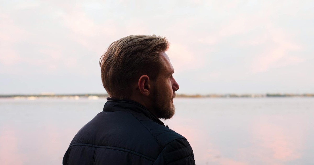 A serene side profile shot of a man gazing over a calm lake at sunset, capturing a moment of reflection.