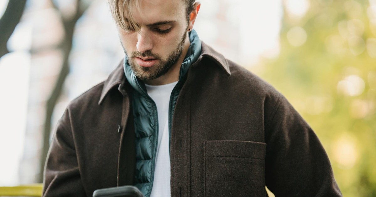 Young bearded man in casual clothes receiving text message on smartphone while standing on street