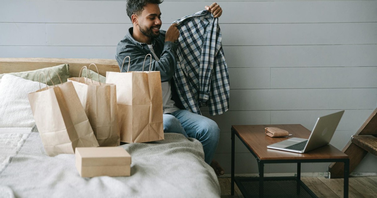A man delightedly examines his new shirt after online shopping in a cozy room setting.