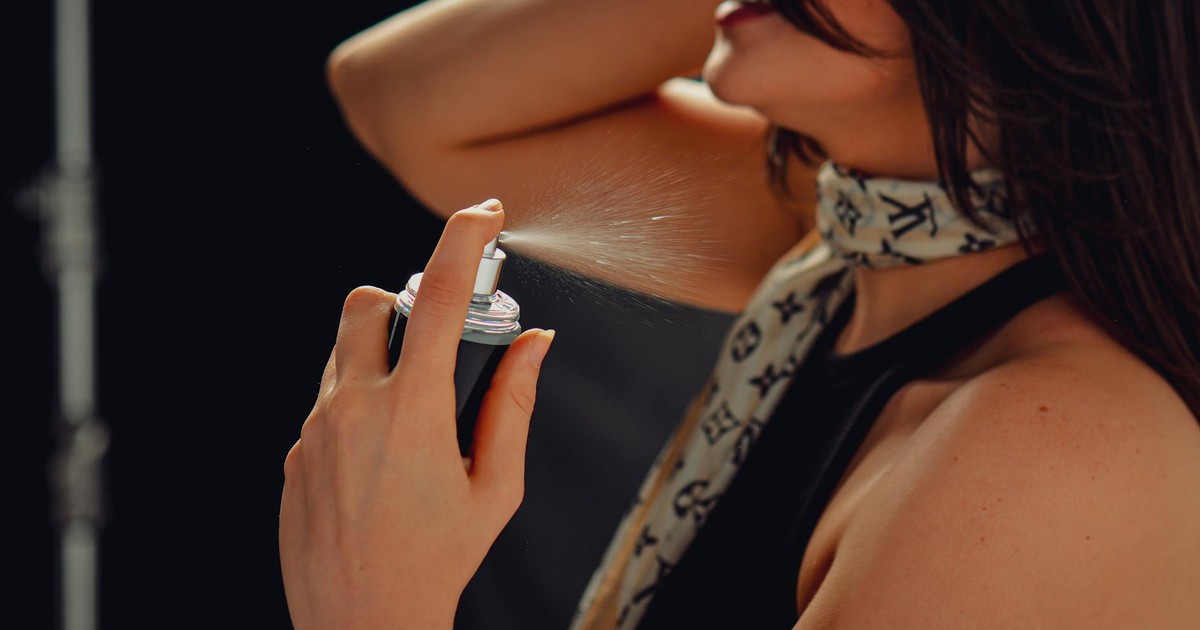 Woman with long hair spraying perfume on her neck, close-up view for a fresh and stylish image.