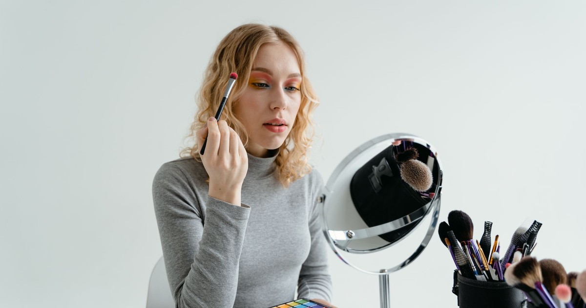 Young woman applying makeup with brush and palette in front of mirror.