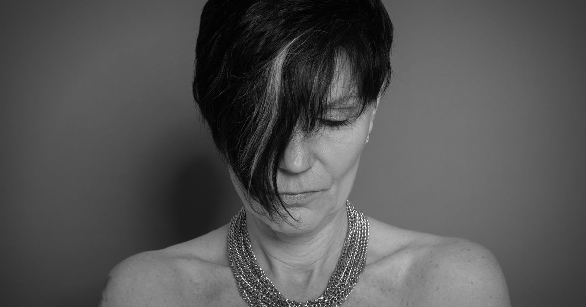 Monochrome portrait of a woman with short hair and chain necklace, eyes closed.
