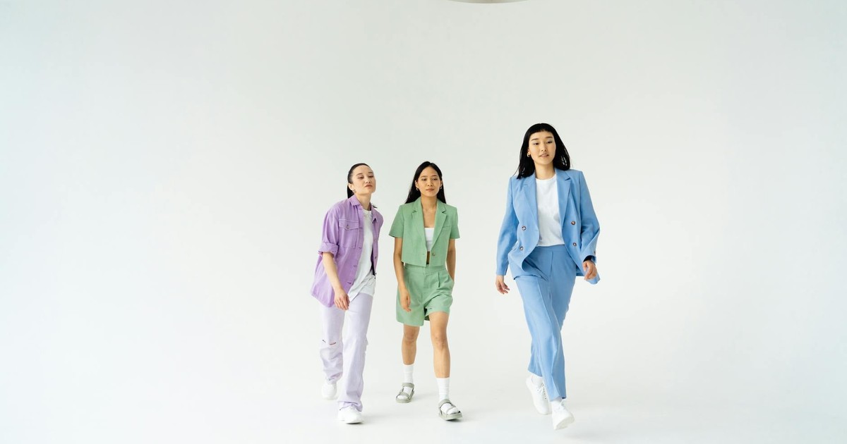 Three young women in trendy pastel suits walking confidently in studio with white background.