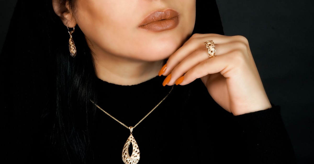 Close-up of a woman adorned in an elegant gold jewelry set, featuring a necklace, earrings, and ring.