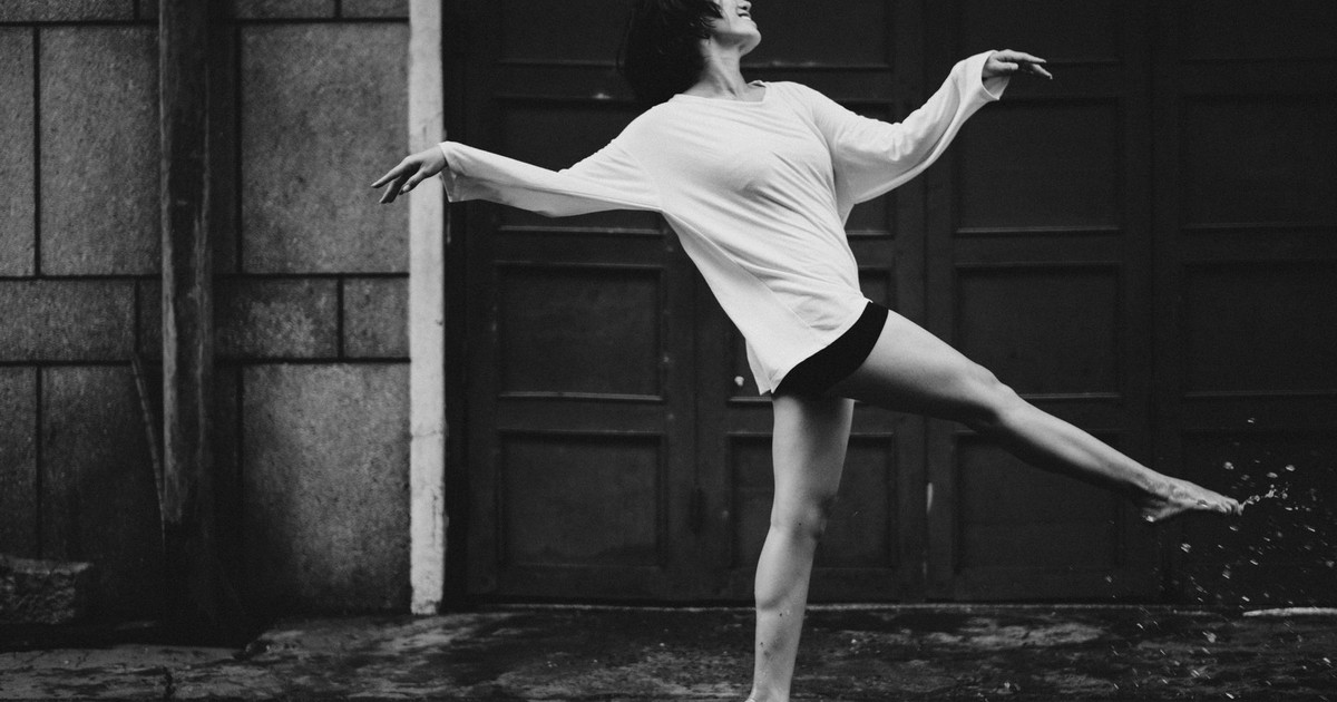 Black and white full body side view of barefoot female dancer walking happily in puddle on street