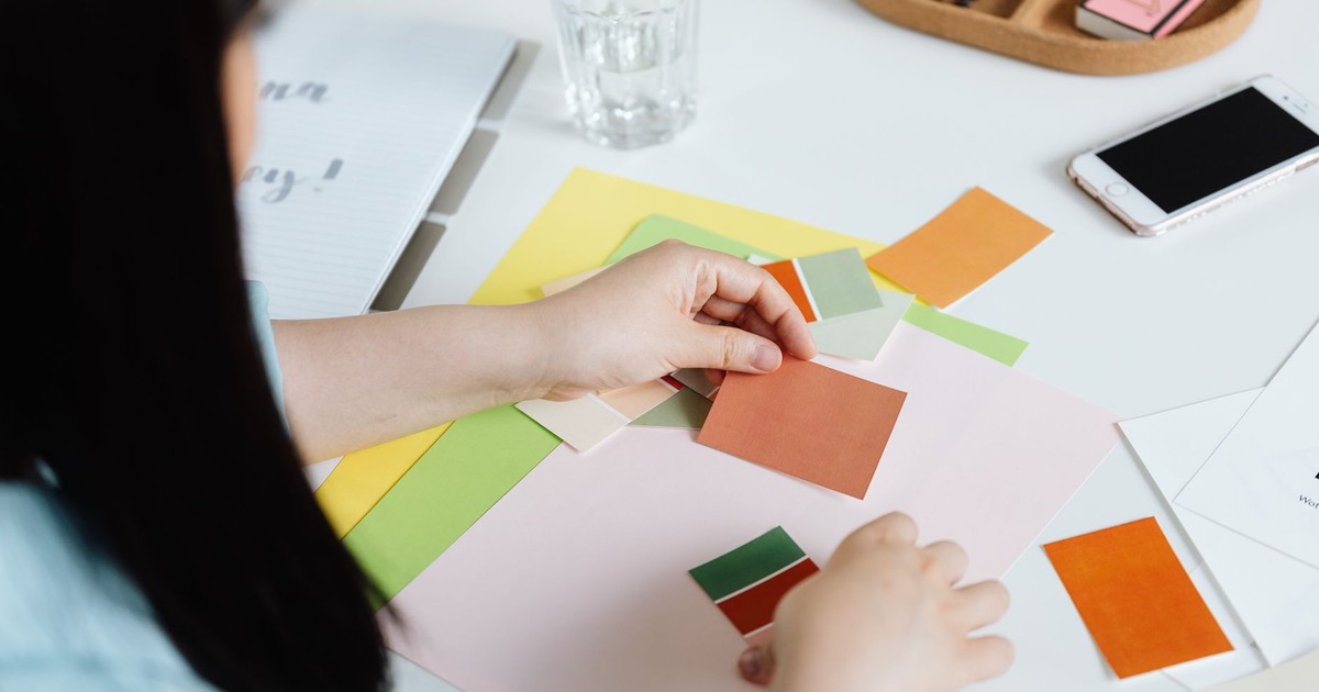 An interior designer arranging color swatches on a desk with a smartphone nearby.