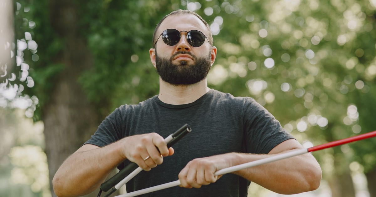 A visually impaired man uses a white cane while outdoors, indicating independence.