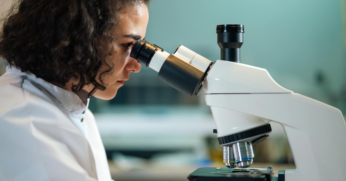 A focused scientist examines samples under a microscope in a laboratory setting.