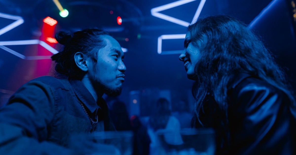 A couple enjoys a night out, conversing under vibrant neon lights in a stylish bar.