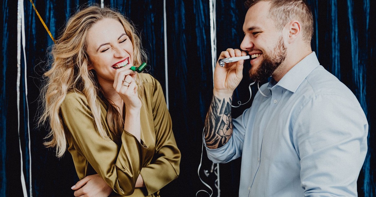 A joyful couple laughing and celebrating indoors with party favors and streamers.