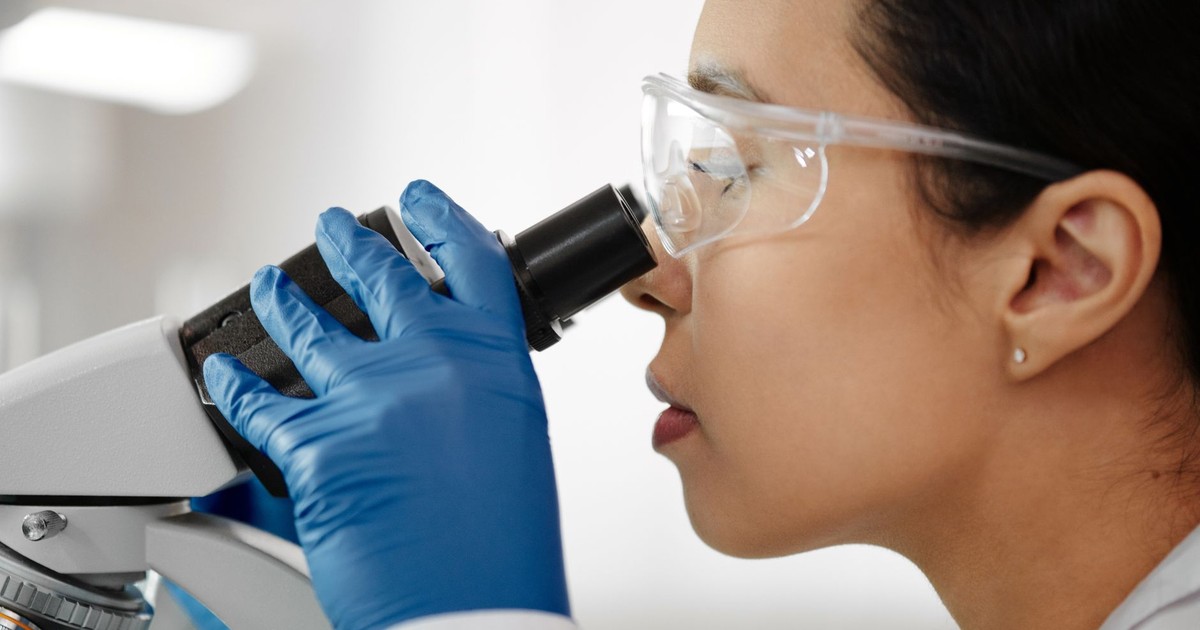 Scientist wearing safety glasses and gloves while examining samples with a microscope in the laboratory.