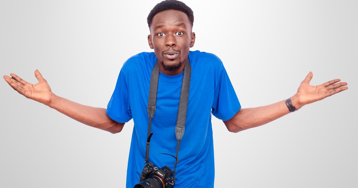 A man with a camera around his neck shrugging in confusion.