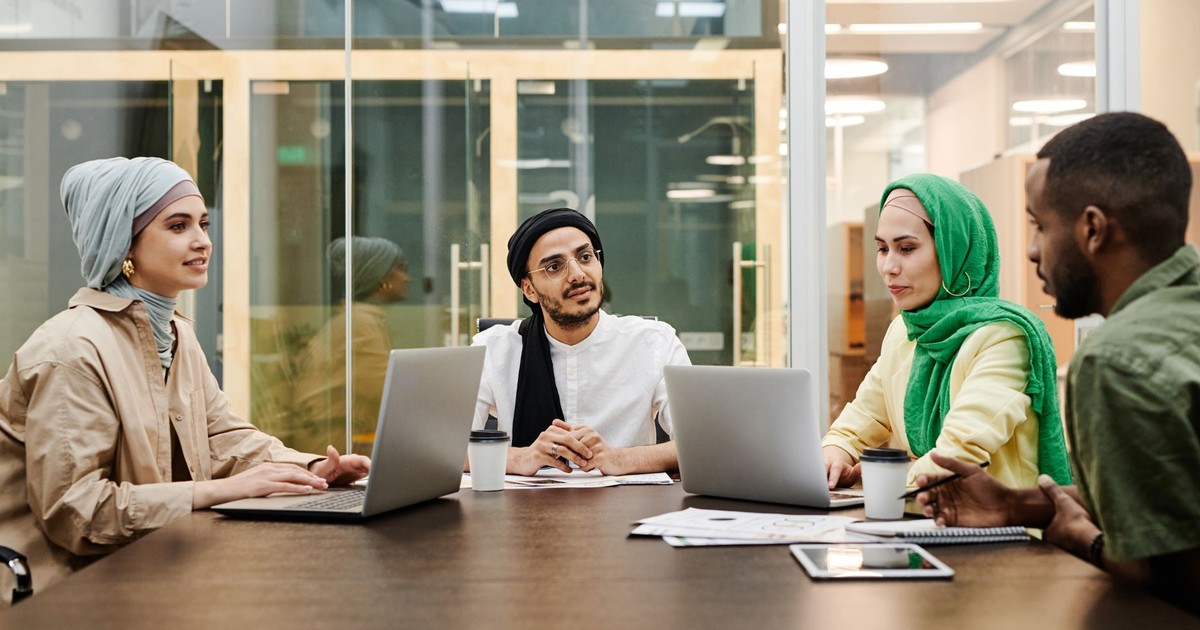A diverse group discussing ideas in a modern office setting, using laptops and tablets.
