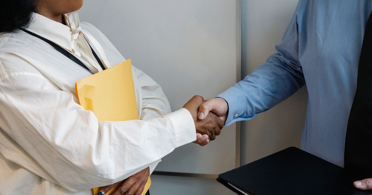 Crop unrecognizable multiethnic colleagues standing with documents and shaking hands while greeting each other in office