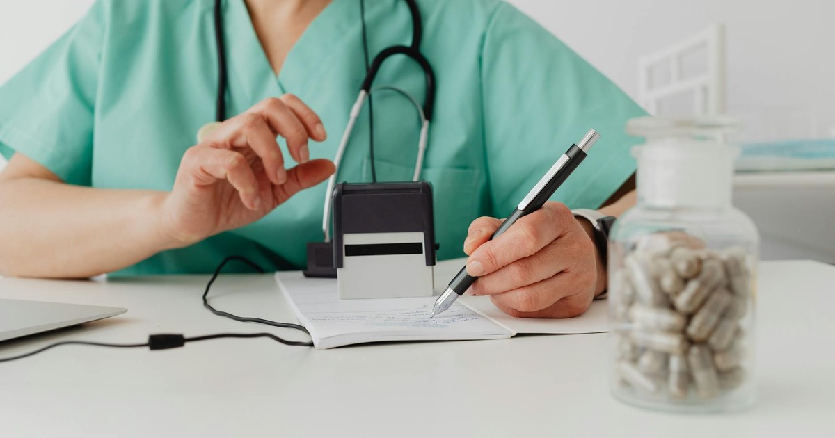 A medical professional writing a prescription in a clinical setting.