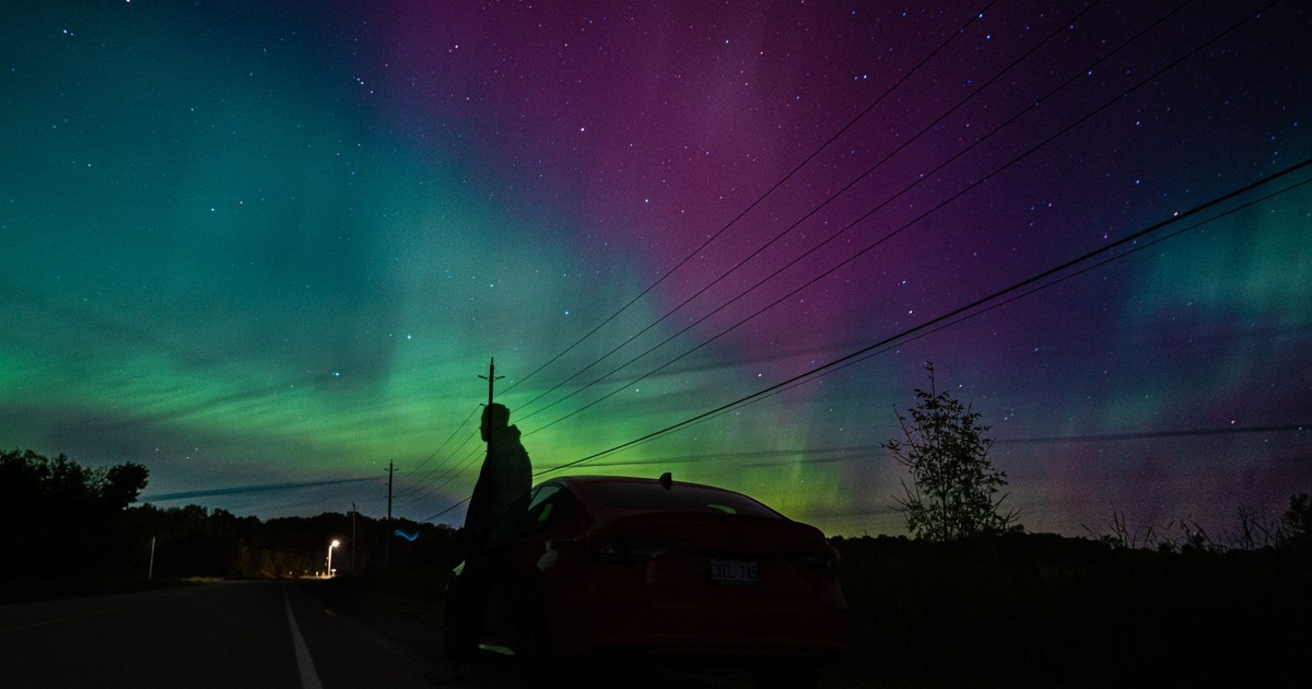 A person stands by a car viewing the vibrant aurora borealis in Ontario, Canada.