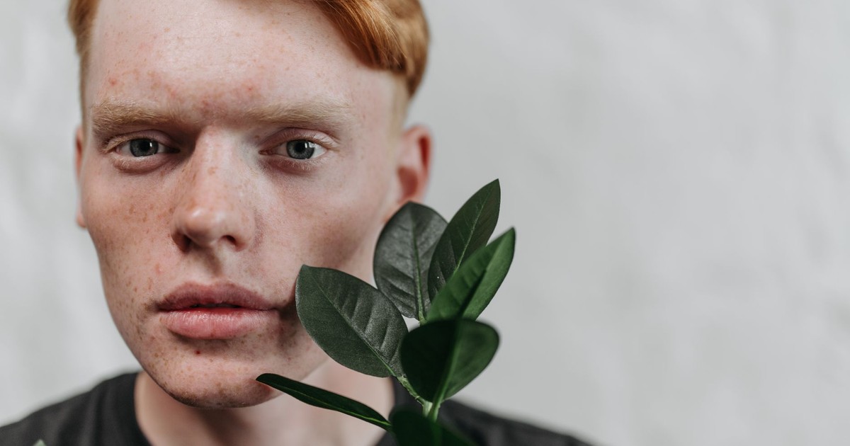 A detailed close-up portrait of a young man with red hair, accented by green leaves, in a studio setting.