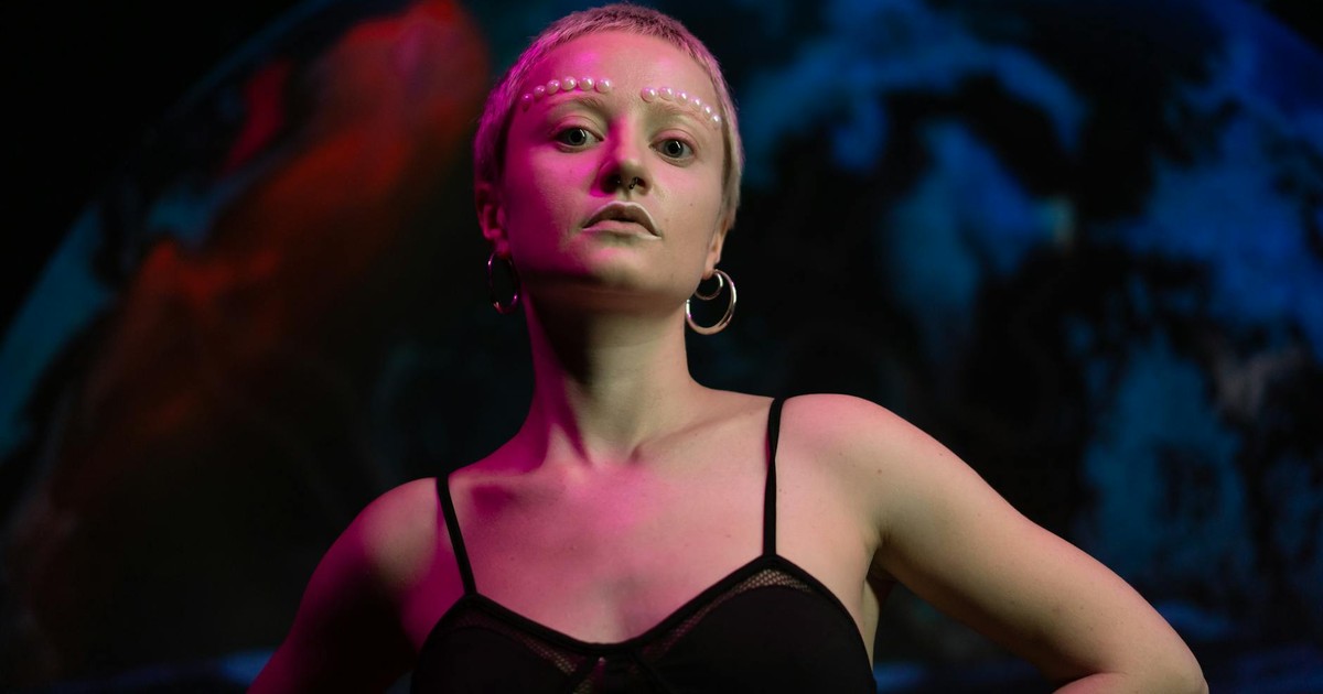 Creative portrait of a woman with white face paint and hoop earrings against a cosmic background.