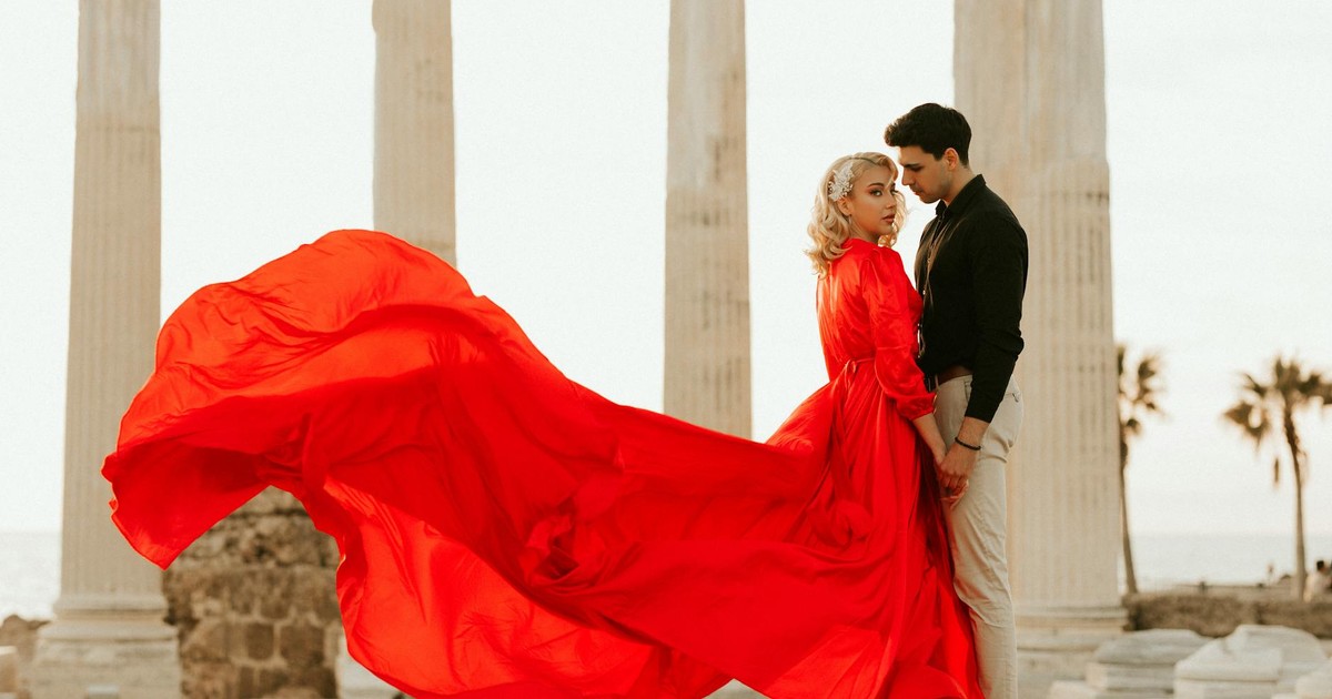 Elegant couple in a red dress sharing a romantic moment amidst ancient ruins.