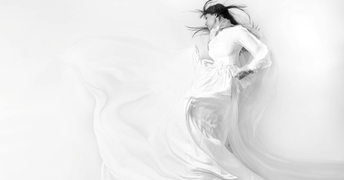 Elegant black and white photo of a woman in a flowing white dress, eyes closed.