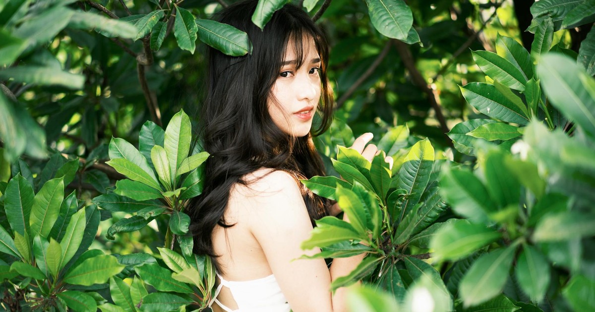 Woman in a white dress standing amidst lush green leaves, capturing serene beauty in nature.