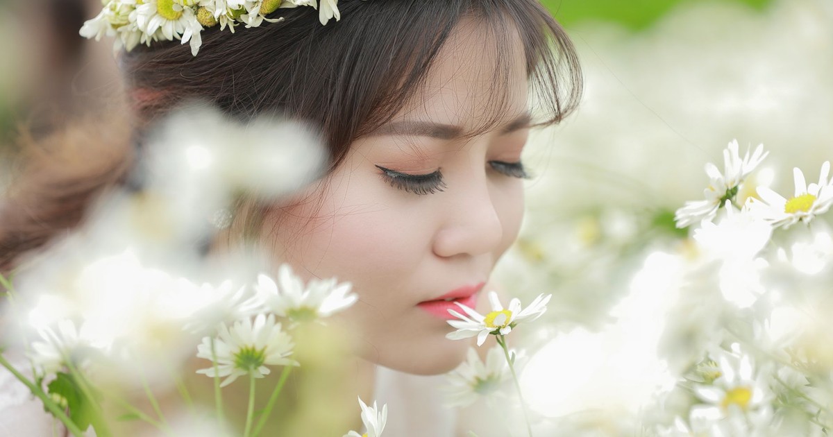 Serene portrait of a woman with a flower crown enjoying daisies in a field.