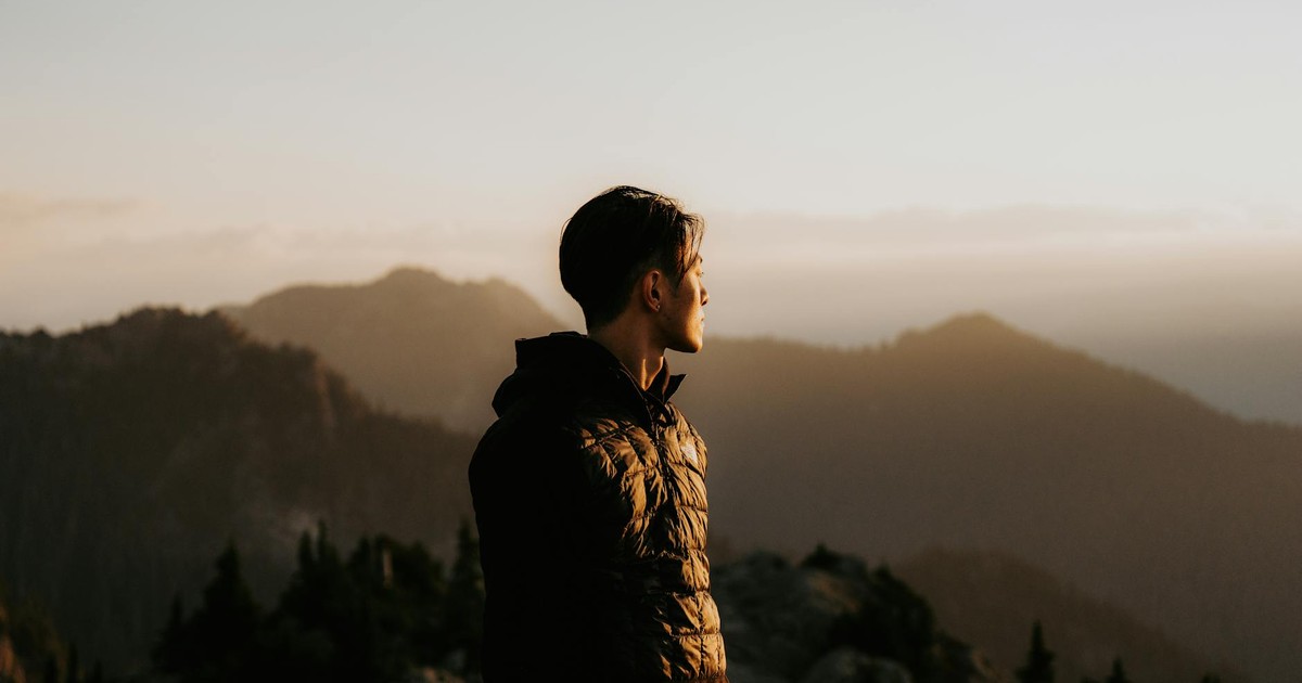 A man overlooks misty mountains at sunset, embracing adventure.
