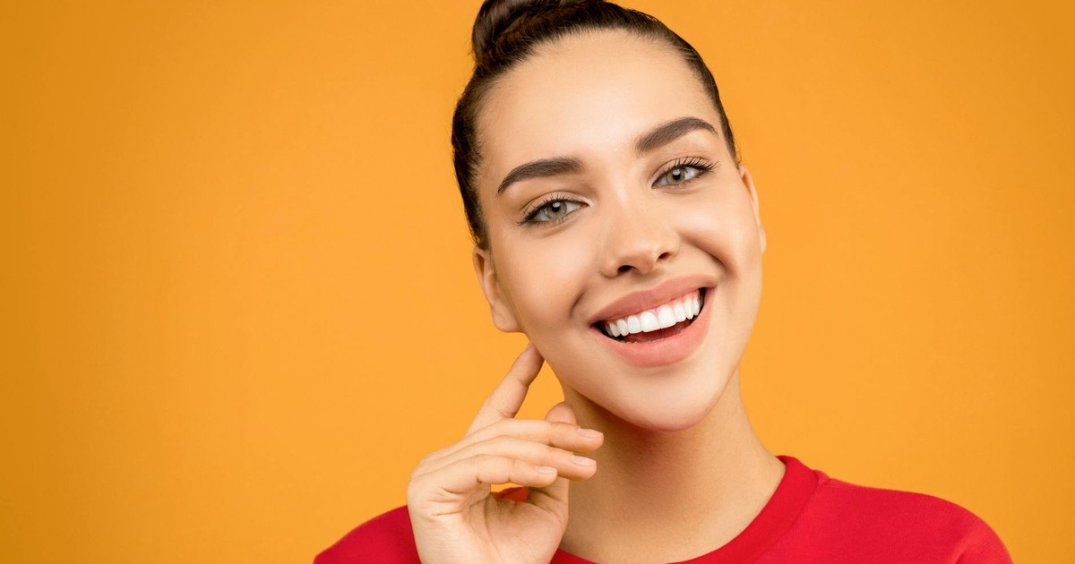 Portrait of a smiling woman in a red top with an orange backdrop, showcasing beauty and joy.