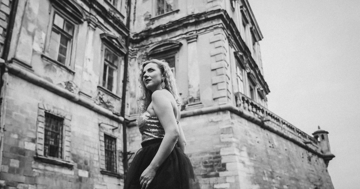 Elegant woman in stylish dress poses by a neoclassical building exterior.
