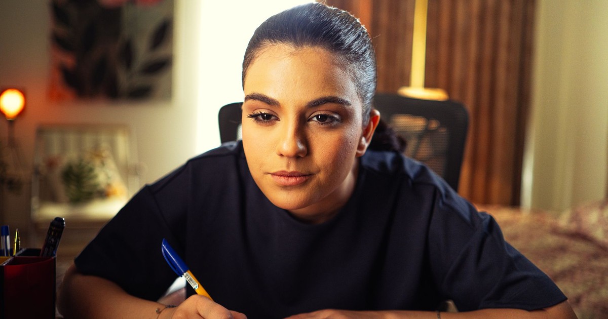 Portrait of a focused woman working at a desk indoors, surrounded by warm lighting.