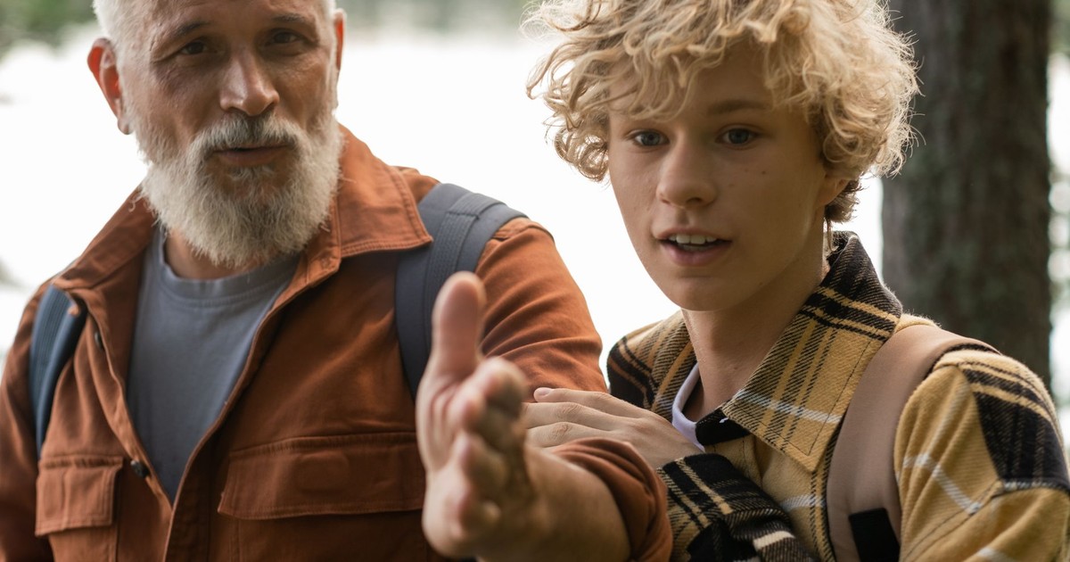 A grandfather guides his grandson through a scenic forest hiking path during summer.