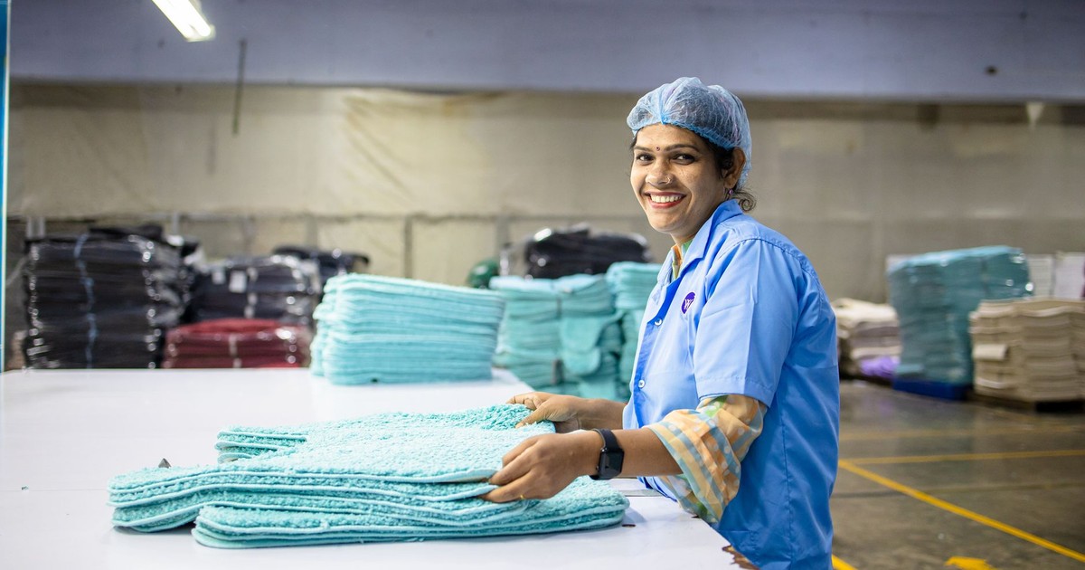 A happy textile worker in a factory is seen folding fabrics, showcasing industrious work environment.