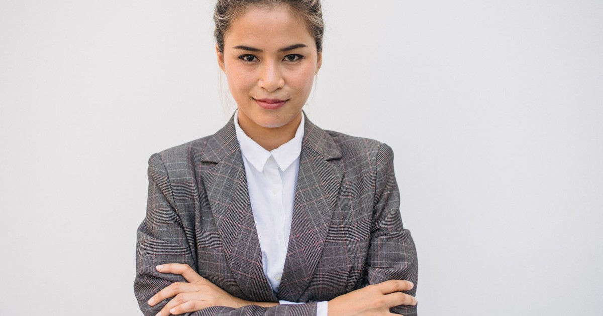 Portrait of a confident Asian woman in a plaid blazer with arms crossed, smiling and posing.