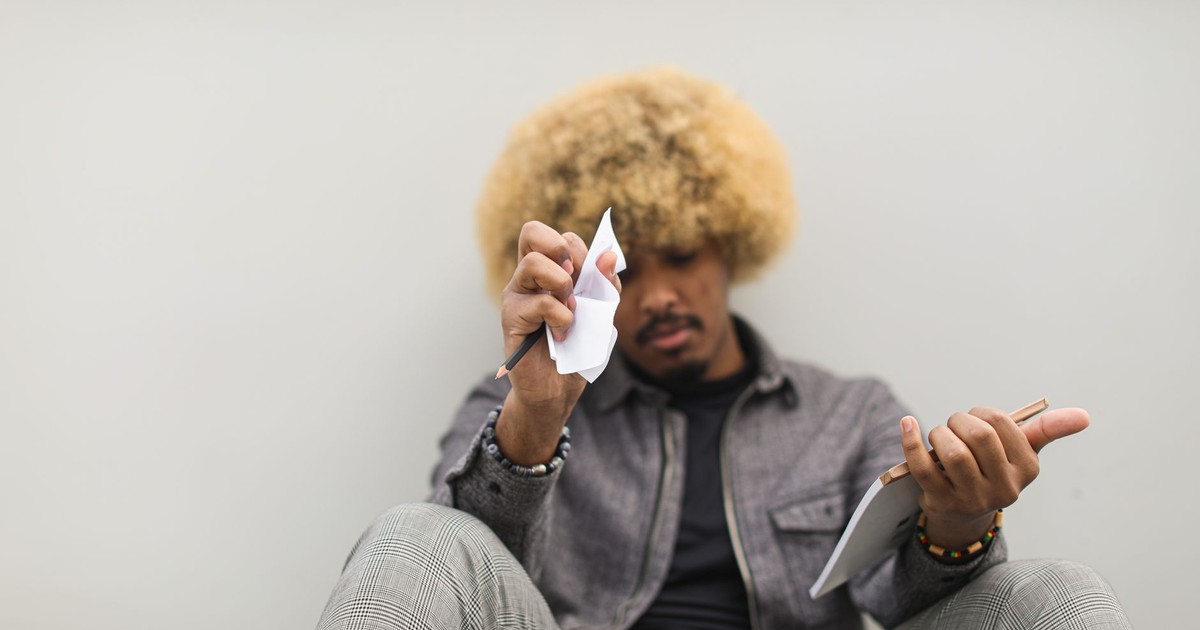 Man sitting with thoughtful expression, holding torn paper and a notebook. Indoor shot.