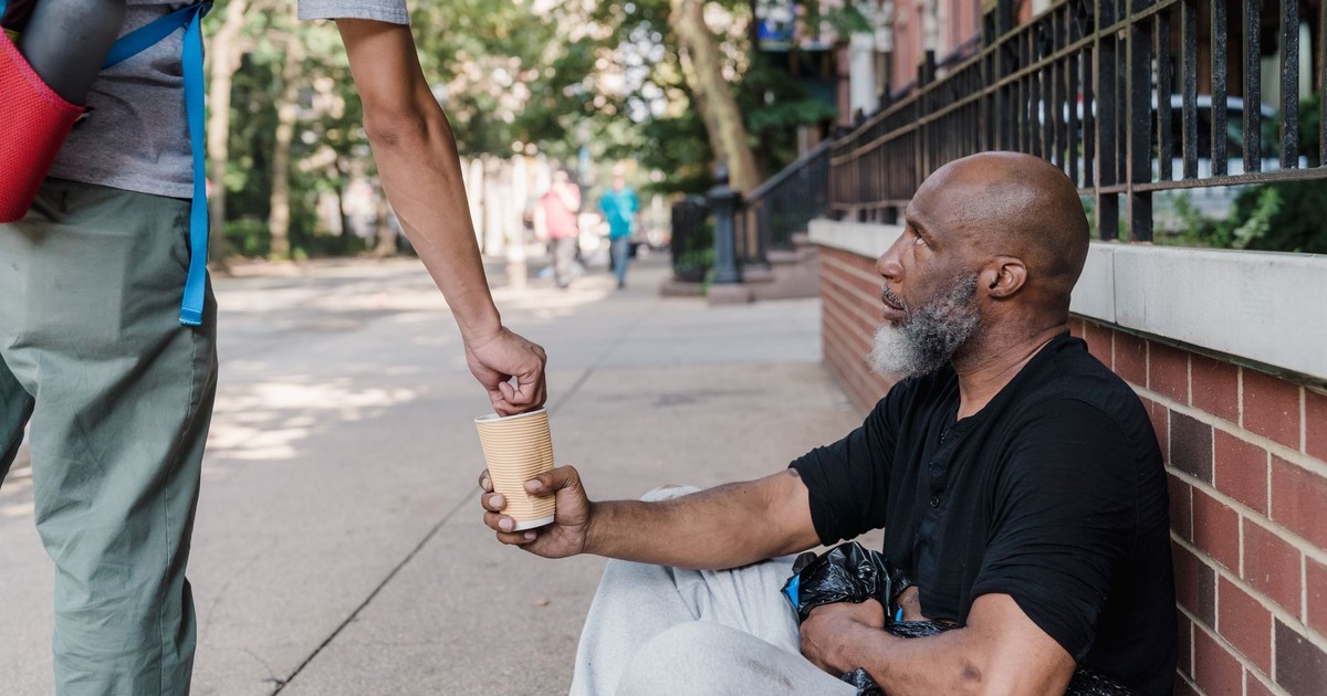 A person offers money to a homeless man sitting on the sidewalk, highlighting urban compassion.