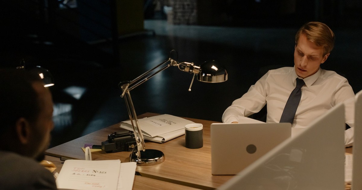 Two professionals working late in an office, reviewing documents under a desk lamp.