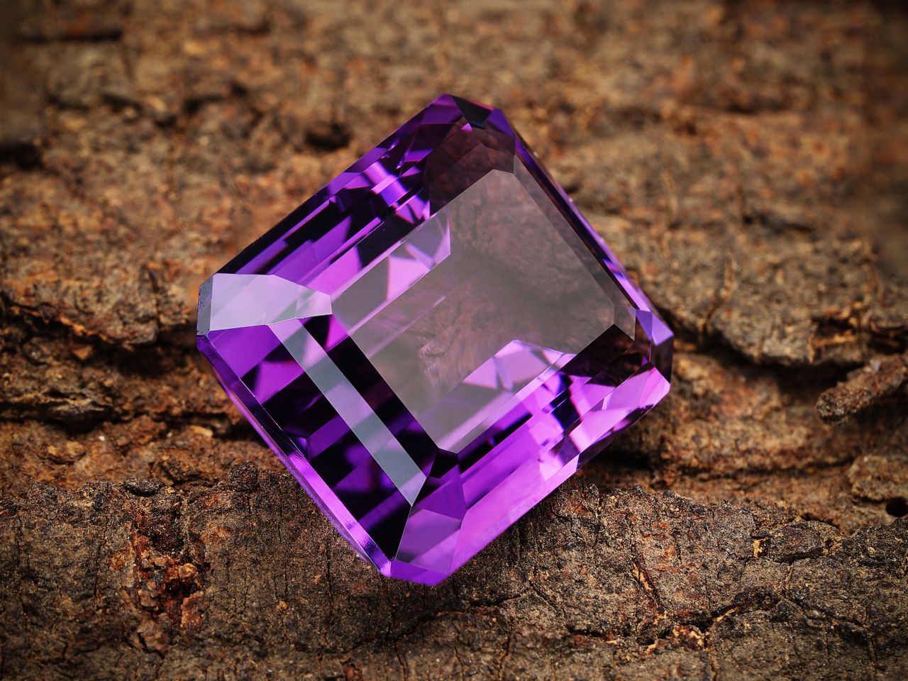 Close-up of a vibrant purple amethyst gemstone resting on a textured brown background