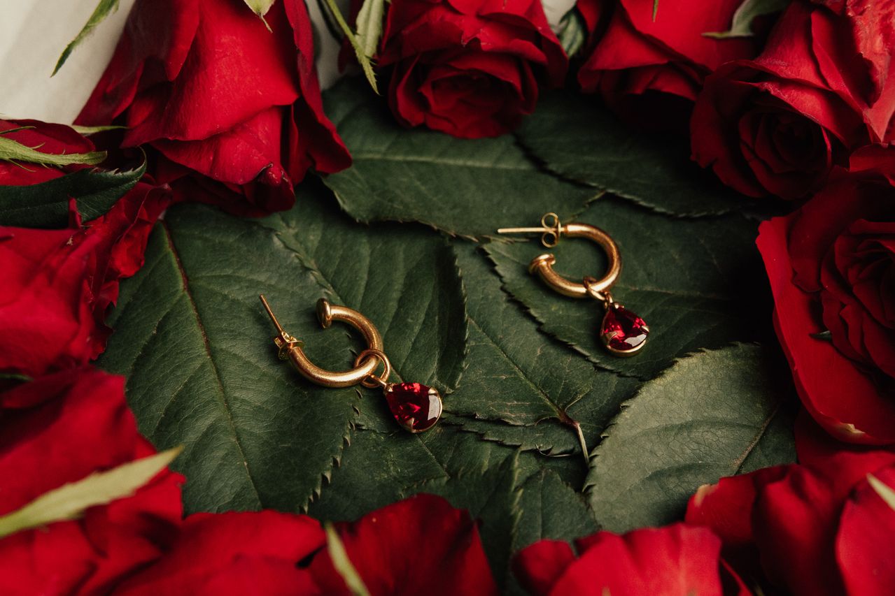 Elegant gold earrings with red gemstones amidst lush red roses on green leaves