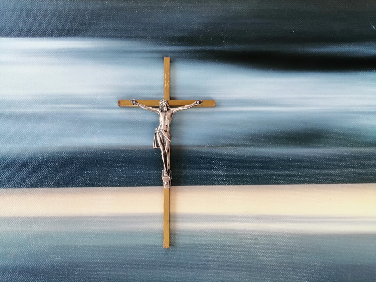 Metal crucifix against a blurred abstract blue and white background, symbolizing faith and spirituality