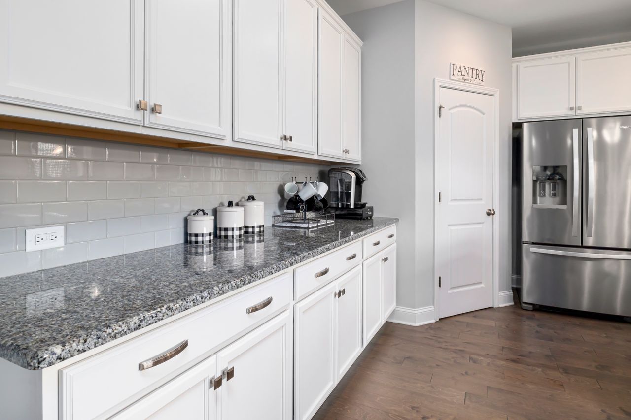Sleek white kitchen with granite countertops and stainless steel appliances, featuring a pantry door